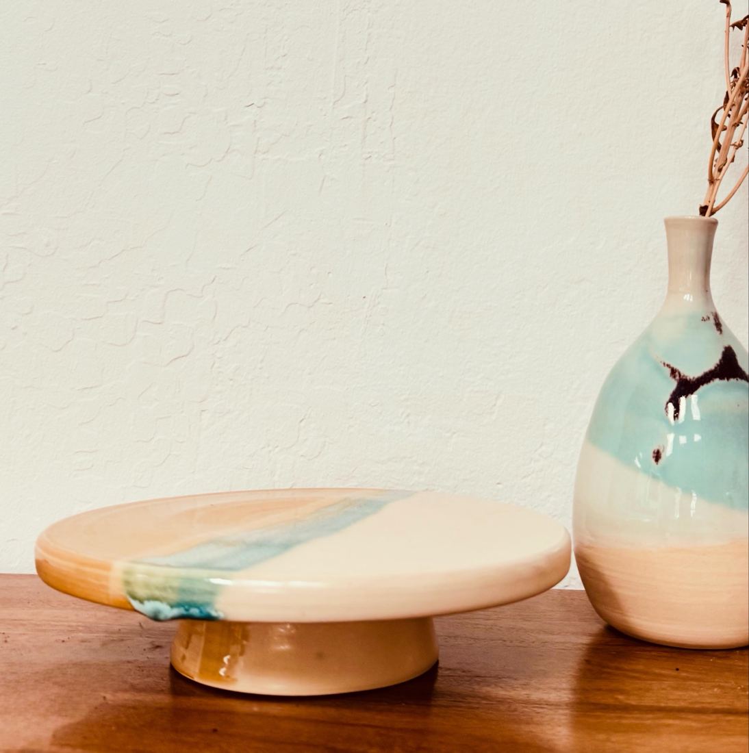 Footed cake stand with a turquoise brushstroke beside a bottle vase