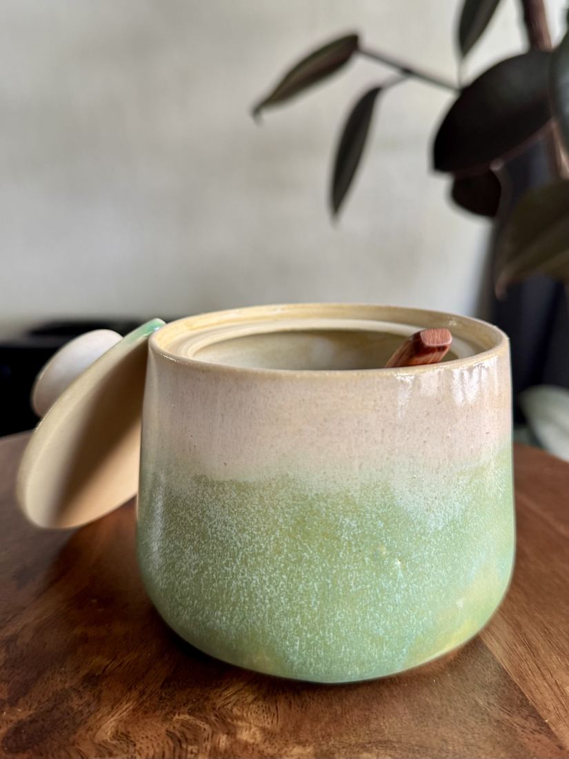 Lidded jar with sage-green ombré glaze and a small wooden spoon