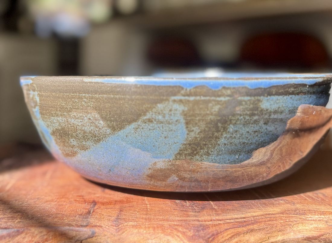 Wide shallow bowl with blue glaze over toasted clay