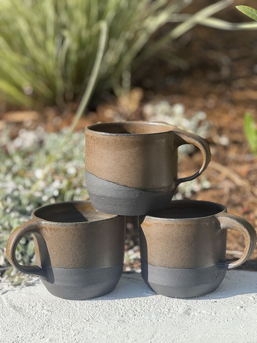 Mugs glazed toasted brown over charcoal, stacked outdoors