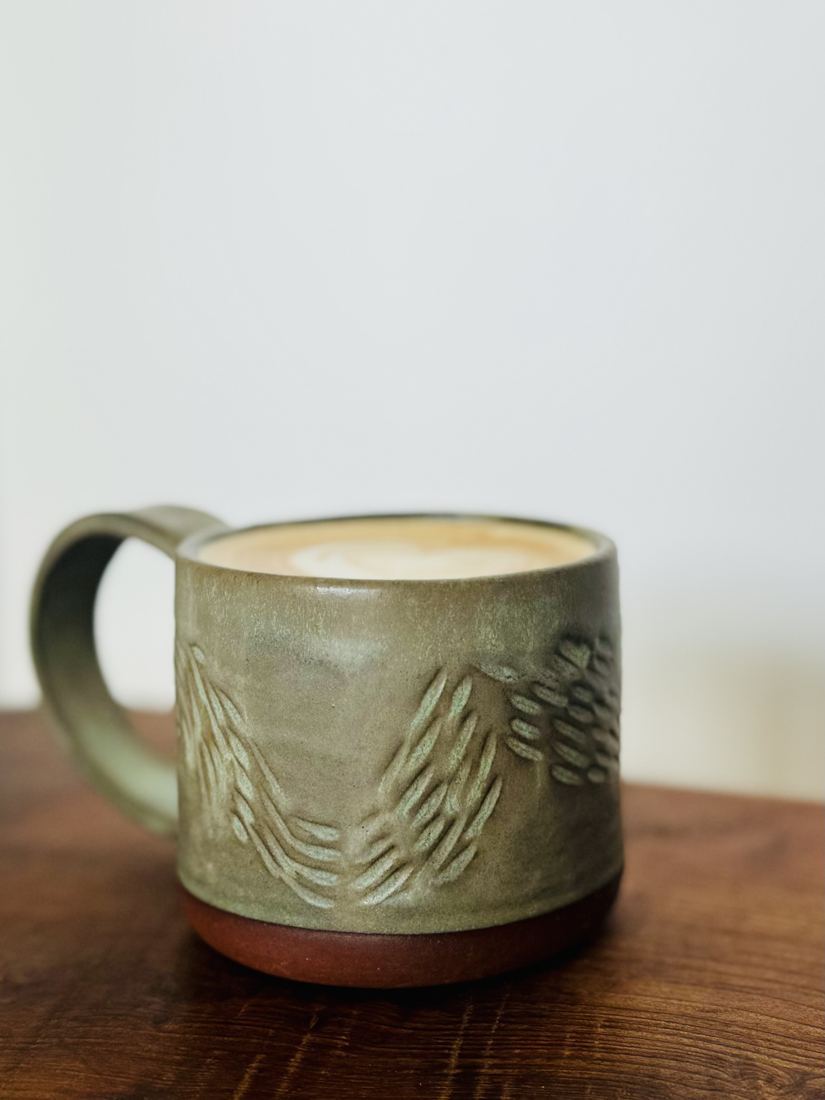 Sage green mug with carved leaf pattern on raw clay foot